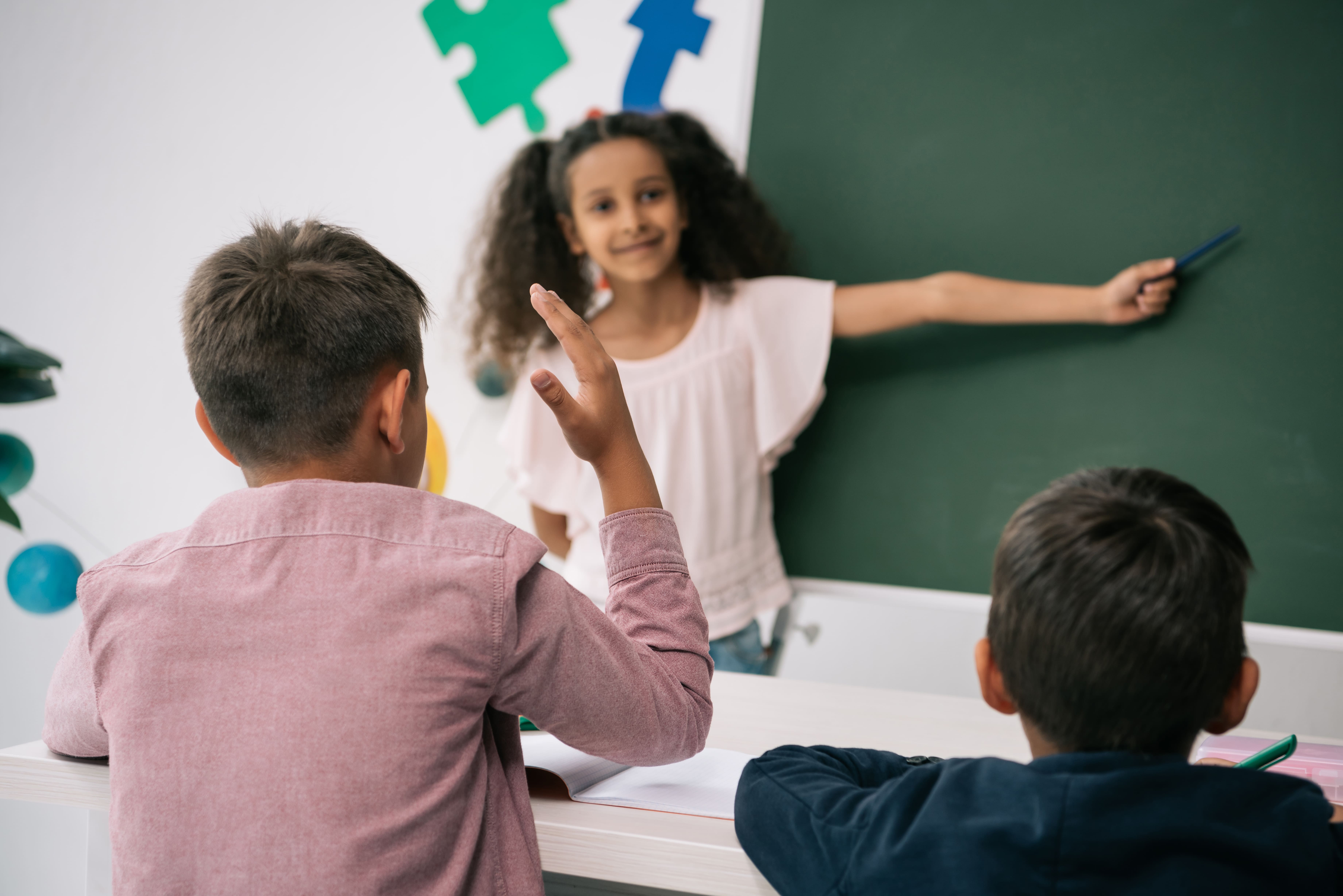 school boy raising his hand and looking at black board