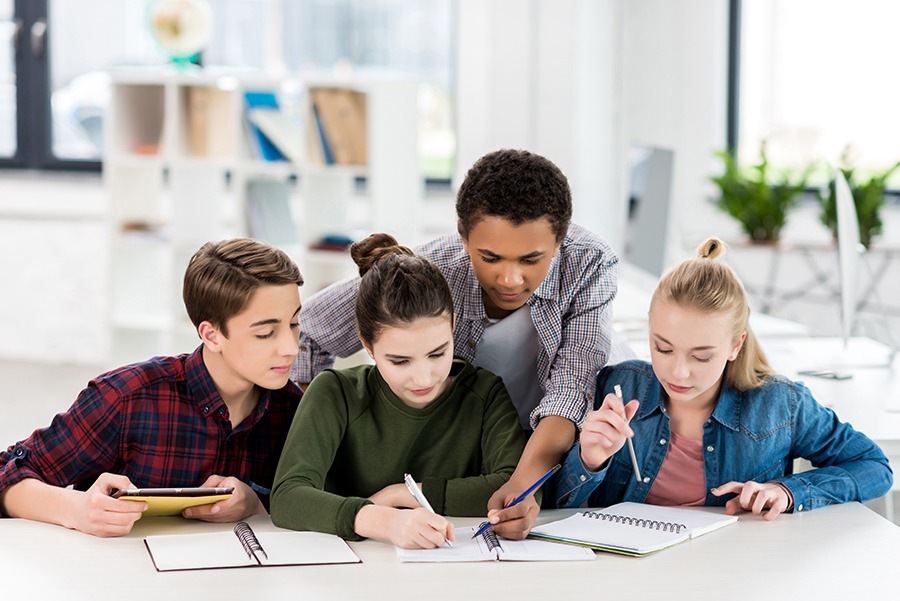 multiethnic group of teenagers doing homework together in class